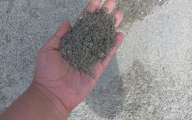 Muestra de arena fina en la mano, sobre el acopio